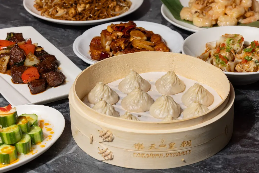 A steamer of xiao long bao with shared plates on a marble table