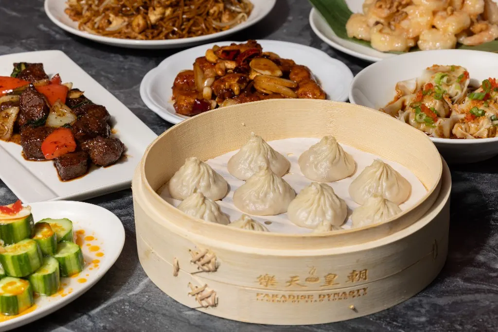 A steamer of xiao long bao surrounded by shared plates