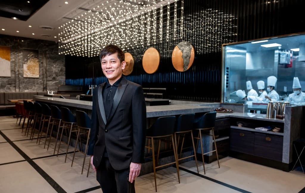 A host in the Paradise Dynasty dining room, with chefs working in the open kitchen